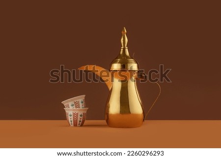 Arabian coffee with golden dallah on a dark red background, A still life of Arabic traditional coffee pot or Dallah of ramadan served with saudi sweet dates.  Royalty-Free Stock Photo #2260296293