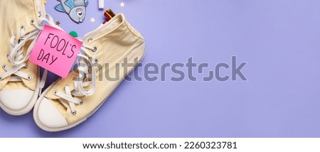 Pair of shoes and sticky note with text FOOL'S DAY on lilac background with space for text