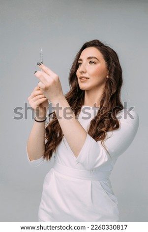 young woman doctor in a white coat holds an insulin syringe in her hand. Girl cosmetologist preparing to make an injection of botulinum toxin in a cosmetology clinic Royalty-Free Stock Photo #2260330817