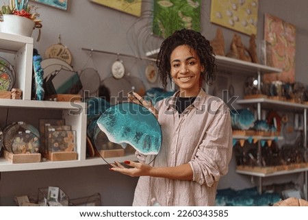Happy woman decorator holding handmade epoxy resin glass tray with sea waves standing in own studio Royalty-Free Stock Photo #2260343585