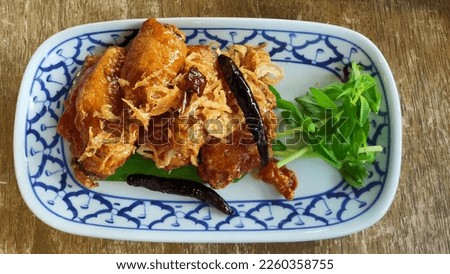 Glazed crispy chicken wings, doused in sticky, sweet and sour sauce. Topped with fried shallots and fried dried chili. Thai food, entree dish, starter plate. Royalty-Free Stock Photo #2260358755