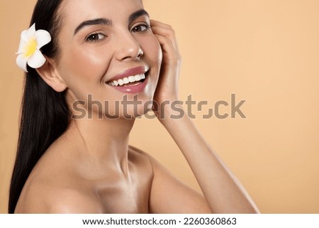 Young woman with plumeria flower in hair on beige background, space for text. Spa treatment