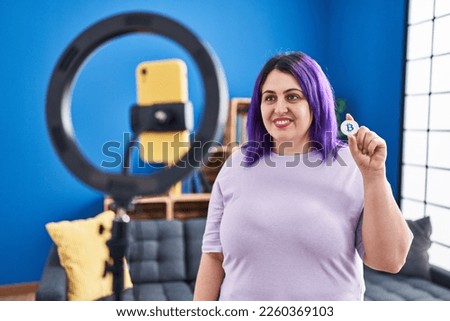 Plus size woman wit purple hair recording bitcoin tutorial with smartphone at home looking positive and happy standing and smiling with a confident smile showing teeth 
