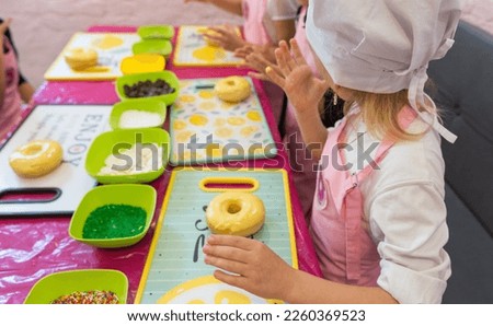 a girl licks her fingers at a donut making workshop. on the table a yellow donut and ingredients in plates for cooking Royalty-Free Stock Photo #2260369523