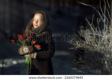 cute caucasian girl wearing warm coat, wool mittens and shawl holding bunch of tulips on cold winter day. Image with selective focus