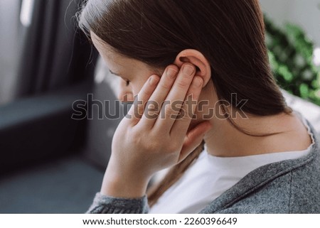 Tinnitus concept. Close up up of sick young caucasian female touch plug ear suffer from noisy disturbing sound sitting on sofa at home. Annoyed millennial lady having earache, hearing problems Royalty-Free Stock Photo #2260396649
