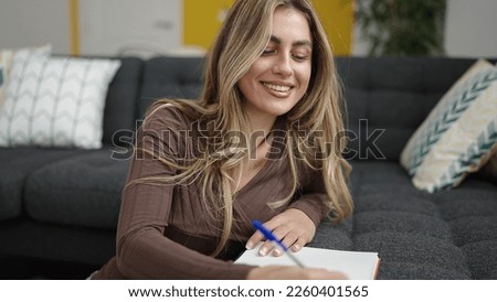 Young blonde woman writing on notebook sitting on floor at home