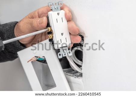 An electrician connects electrical wires to an outlet before installing it. Royalty-Free Stock Photo #2260410545