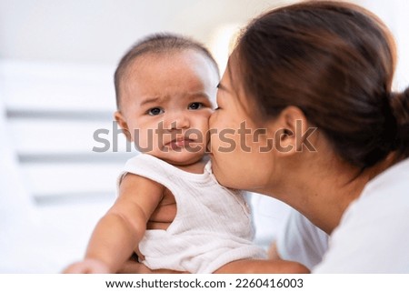 Mom happy joyful teasing asian infant baby new born sitting on bed and kiss her