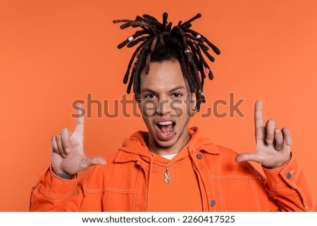 portrait of tattooed multiracial man with dreadlocks looking at camera while showing frame gesture isolated on coral background Royalty-Free Stock Photo #2260417525