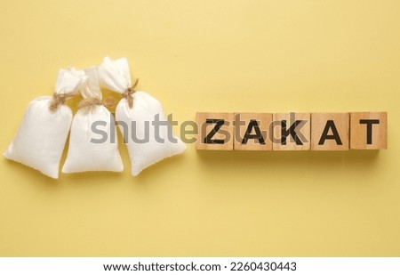 A picture of 3 rice bag with wooden block written "Zakat". Zakat is a religious duty for all Muslims who meet the necessary criteria of wealth to help the needy.