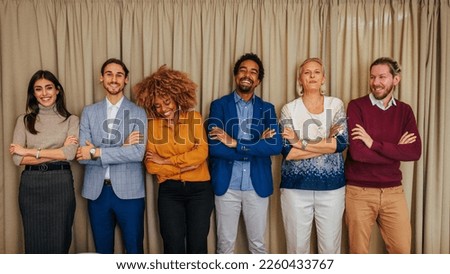 A portrait of a young cheerful business team standing with their arms folded in an office looking at the camera.