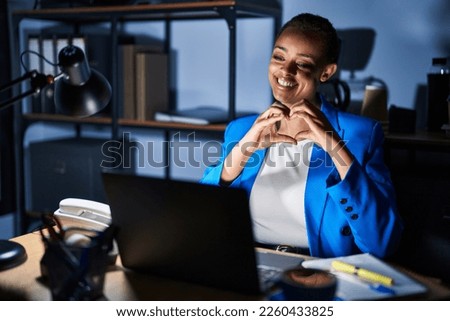 Beautiful african american woman working at the office at night smiling in love doing heart symbol shape with hands. romantic concept. 