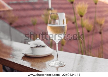 A glass of cold white wine, olives on a wooden table, rooftop background 