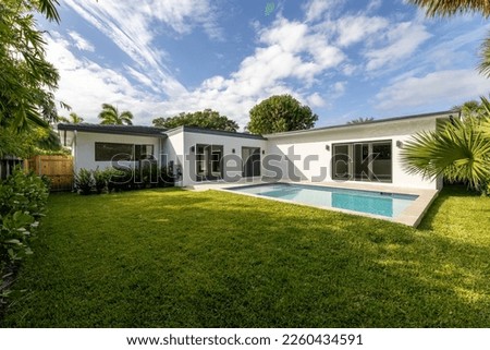 Beautiful backyard of elegant and modern house in the Nautilius neighborhood of Miami Beach, swimming pool, short grass, trees and tropical plants, blue sky in the background