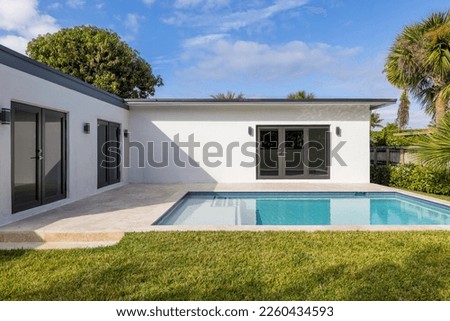 Beautiful backyard of elegant and modern house in the Nautilius neighborhood of Miami Beach, swimming pool, short grass, trees and tropical plants, blue sky in the background Royalty-Free Stock Photo #2260434593