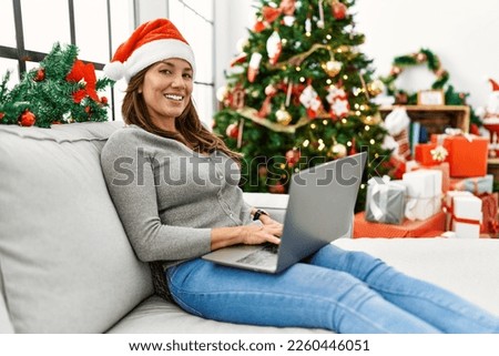 Young latin woman using laptop sitting by christmas tree at home