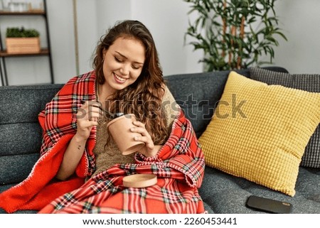 Young beautiful hispanic woman eating ice cream sitting on sofa at home Royalty-Free Stock Photo #2260453441