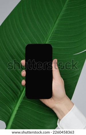 Hand holding empty screen smart phone on tropical green leave background with copy space.