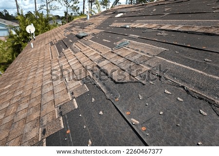 Wind damaged house roof with missing asphalt shingles after hurricane Ian in Florida. Repair of home rooftop concept Royalty-Free Stock Photo #2260467377