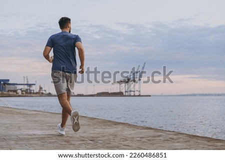Full body back view young strong sporty athletic toned fit sportsman man in sports clothes warm up training run jog at sunrise sun over sea beach outdoor on pier seaside in summer day cloudy morning. Royalty-Free Stock Photo #2260486851