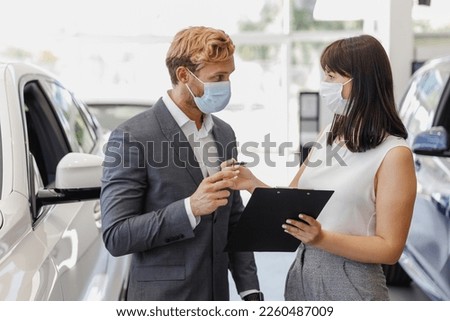 Man customer buyer client in suit pandemic masks choose auto want buy new car automobile in showroom consult with salesman signs documents vehicle salon dealership store motor show indoor Sale concept