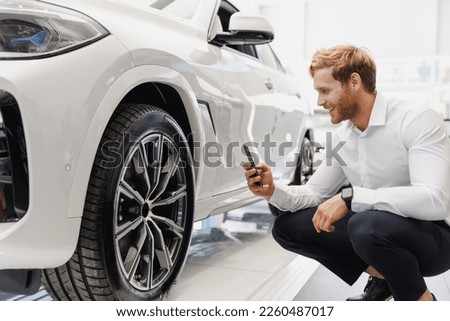 Man customer buyer client in shirt take photo of tire wheel disc mobile cell phone choose auto want buy new car automobile in showroom salon vehicle dealership store motor show indoor Sales concept.
