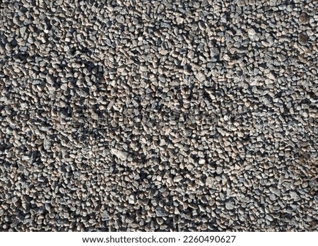Small dark grey cinder stones lie on a dirt road, top view in the rays of the midday sun.