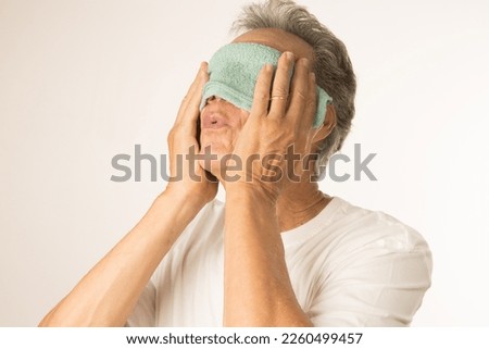 Older man with a warn compress over his eyes for pain relief Royalty-Free Stock Photo #2260499457