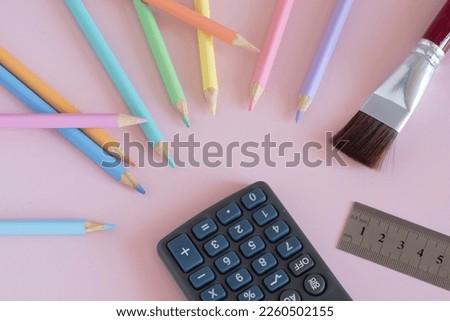 Pastel colored pencils with a brush and a calculator, top view on pink background, back to school concept