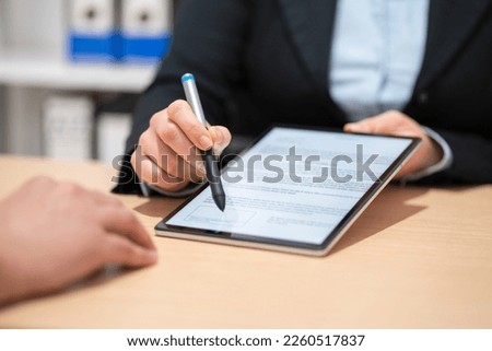 Close up of an executive hands holding a pen with digital tablet and indicating where to sign a contract at office