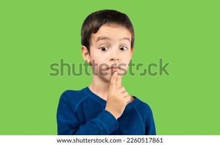 Pensive child looks away at copy space thinking isolated on a green background, funny kid lips hold finger near mouth conceiving some kind of joke, conceptual image Royalty-Free Stock Photo #2260517861