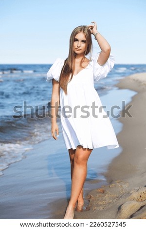 Happy, beautiful woman on the ocean beach standing in a white summer dress.