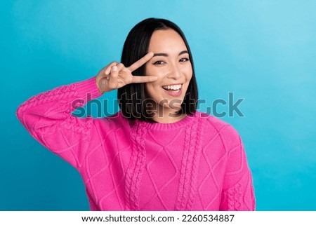 Photo of cheerful thai person beaming smile hand fingers show v-sign near eye isolated on blue color background