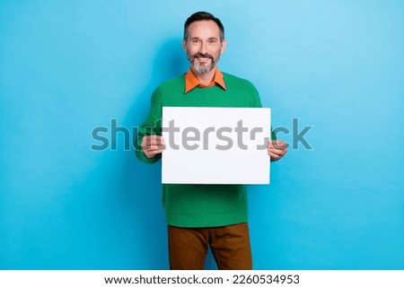 Photo of mature aged promoter man wear green sweater orange shirt hold paper empty space banner new offer isolated on blue color background