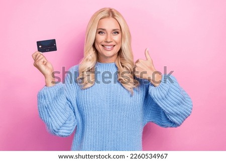 Photo of adorable positive woman with curly hairstyle wear blue sweater hold plastic card show thumb up isolated on pink color background