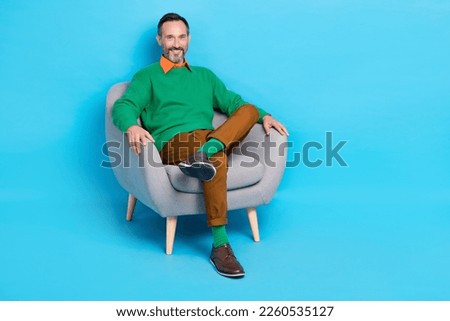 Full length photo of mature nice mister sitting comfy soft armchair relaxing dressed stylish green look isolated on blue color background Royalty-Free Stock Photo #2260535127