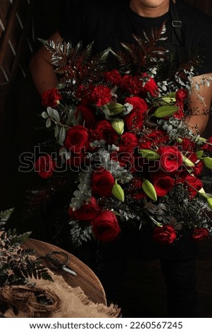 a man carrying a bouquet of flowers, a combination of red roses, lilies and some beautiful leaves into a bouquet