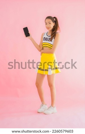Portrait beautiful young asian woman cheerleader with smart mobile phone on pink isolated background