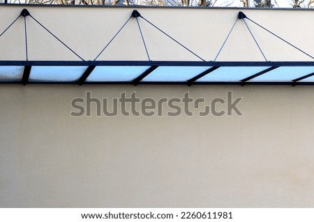 glass shelter by a beige historical building. attached to the facade of the wall in a metal frame suspended on rod rods. struts on the pivot pin. protects the entrance area from rain and snow, glass