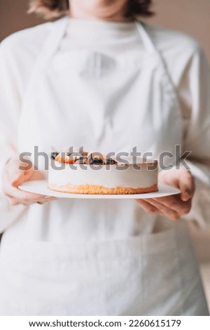 Lady pastry chef in white apron holding bird's milk cake in her hands.