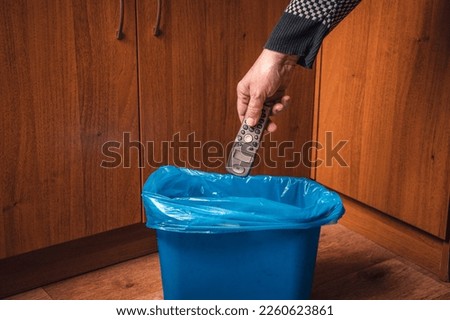 A man throws an old push-button radiotelephone into a trash can. Man's hand with a push-button telephone and a trash can in blue. Royalty-Free Stock Photo #2260623861