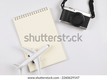 Top view or flat lay of blank page opened notebook, airplane model  and camera on white  background with copy space. Travel, photo and memory concept.