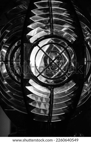Vertical black and white photo of a Lighthouse lamp with a Fresnel lens. It is a type of composite compact lens developed by the French physicist Augustin-Jean Fresnel