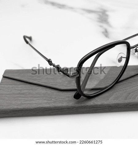 A glasses on a marble table, with some decorations on the side, there is a glasses case next to it,  close up glasses details.
