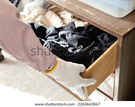Hand with work gloves opening the drawer containing clothes Royalty-Free Stock Photo #2260663867