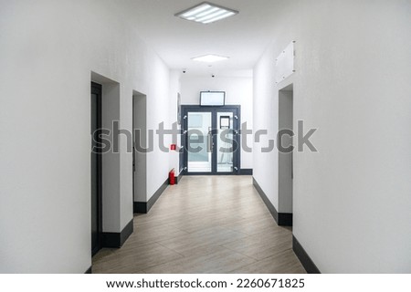 A long narrow corridor of a modern office. Interior design in an office building. Upholstered furniture in the waiting room, glass doors and halogen lamps on the ceiling. Banking sector.