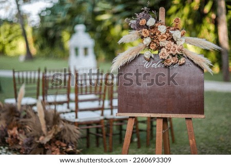 Wooden welcome board sign with a beautiful flower and rustic decoration, standing in front of wedding entrance.