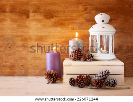 Vintage Lantern with burning Candle and pine cones on wooden table. filtered image 