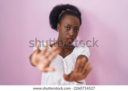 African woman with curly hair standing over pink background doing frame using hands palms and fingers, camera perspective 